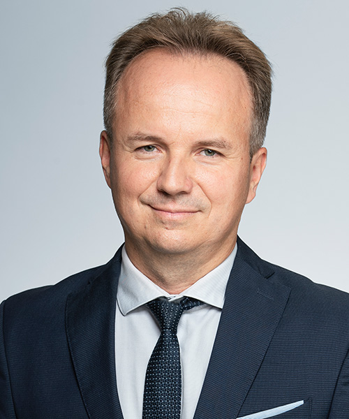 mężczyzna w garniturze i krawacie stoi z poważnym wyrazem twarzy