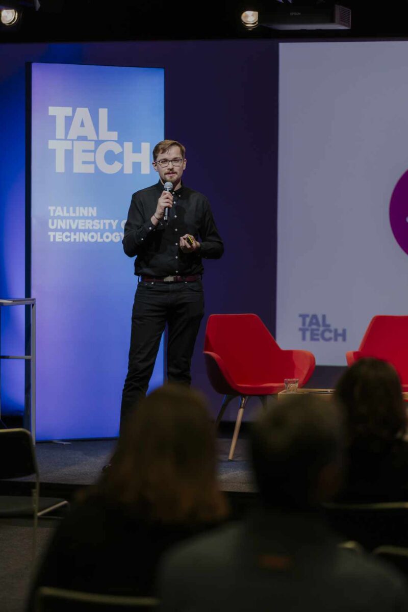 Krzysztof Jeromin występujący na scenie konferencji, w tle ekrany z napisem TAL TECH.