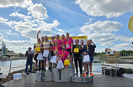 Grupa ludzi na podium z uniesionymi rękami, celebrująca osiągnięcie lub zwycięstwo