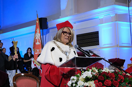 Kobieta w oficjalnym stroju i okularach wygłasza przemówienie