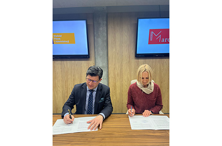 dwie osoby podpisują dokumenty przy stole, obok telewizora